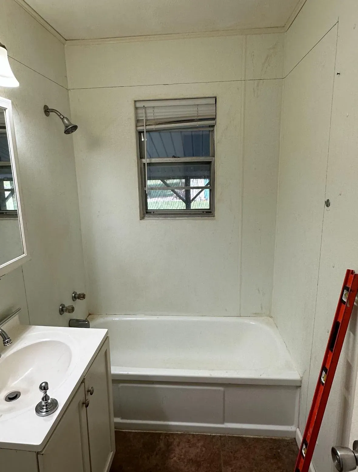 A dated combination shower bathtub with a small window.